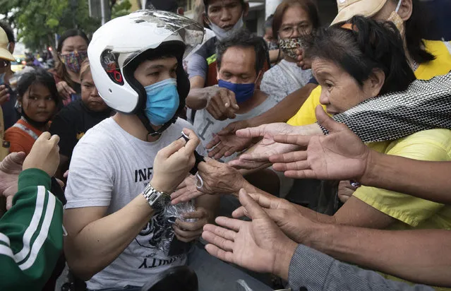 A motorist, white helmet, offers free face masks to locals to help curb the spread of the coronavirus in Bangkok, Thailand on Monday, April 13, 2020. (Photo by Sakchai Lalit/AP Photo)