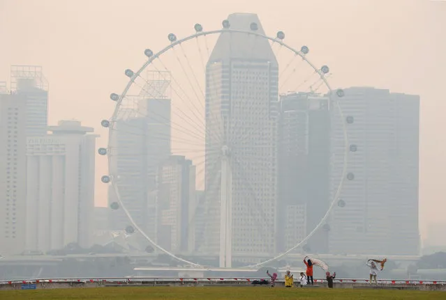 People take photos near the Singapore Flyer observatory wheel shrouded by haze August 26, 2016. (Photo by Edgar Su/Reuters)