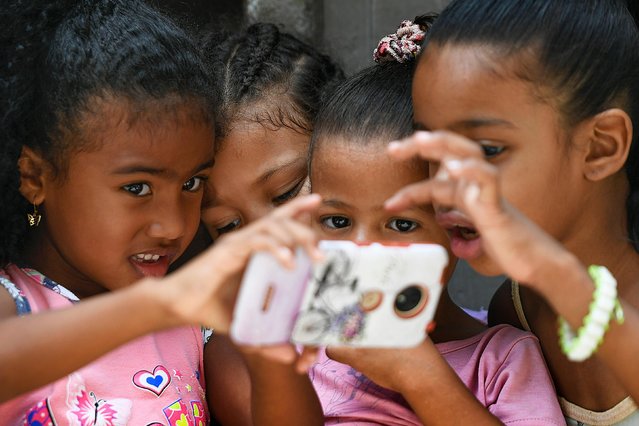 Children play with a smart-phone during the Saint John the Baptist feast in the San Agustin neighborhood of Caracas, Venezuela, Wednesday, June 24, 2020. The traditional feast is celebrated with a procession around the neighborhood with the statue of Saint John the Baptist but the COVID-19 quarantine reduced the feast to a neighborhood meeting. (Photo by Matias Delacroix/AP Photo)