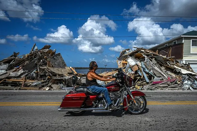 A motorcyclist rides past debris piled up from a destroyed home after the passage of Hurricane Ian on Matlacha Island in Lee County, Florida on November 7, 2022, the eve of the midterm elections. (Photo by Giorgio Viera/AFP Phoot)