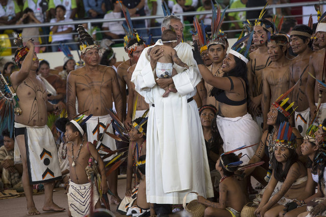 A priest holds a baby as clergy and indigenous people wait for the arrival of Pope Francis in Puerto Maldonado, Madre de Dios province, Peru, Friday, January 19, 2018. Francis is expected to meet with several thousand indigenous people gathering in a coliseum in Puerto Maldonado, the city considered a gateway to the Amazon, in the first full day of the pontiff's visit to Peru. (Photo by Rodrigo Abd/AP Photo)