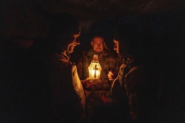 Ukrainian servicemen pray as they receive a Bethlehem Light of Peace from a comrade during Christmas holidays at their position near Kharkiv, Ukraine, Monday, December 26, 2022. (Photo by Evgeniy Maloletka/AP Photo)