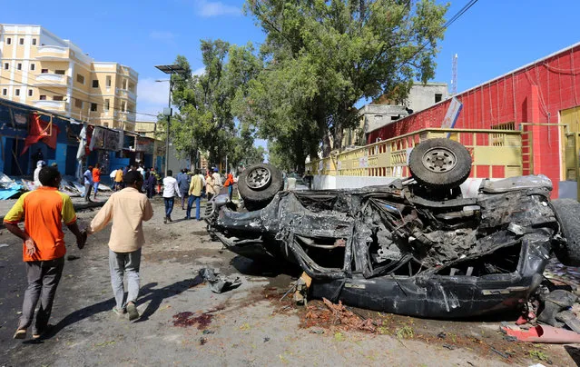 People walk past a car wreckage at the scene of an attack on a restaurant by the Somali Islamist group al Shabaab in the capital Mogadishu, Somalia, October 1, 2016. (Photo by Feisal Omar/Reuters)