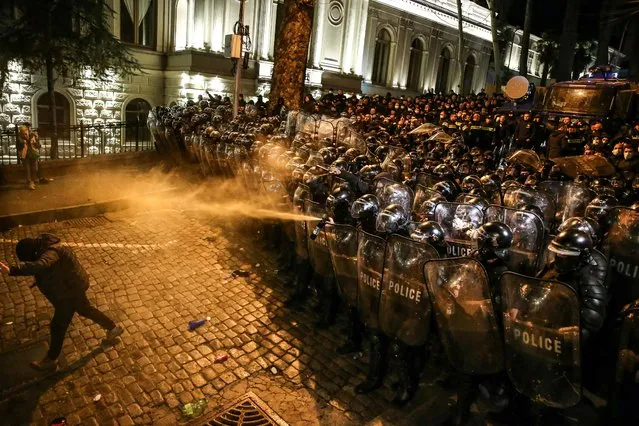 Georgian riot police spray tear gas towards a protester as they form a cordon during clashes with protesters near the Georgian parliament in Tbilisi on March 7, 2023. Georgian police used tear gas and water cannon against protesters Tuesday as thousands of demonstrators took to the streets in the capital Tbilisi to oppose a controversial “foreign agents” bill. (Photo by AFP Photo/Stringer)