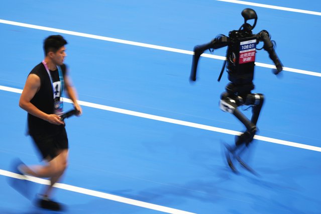 A human operator runs along with a robot in the 1500m event for the World Humanoid Robot Games in Beijing, China, Friday, August 15, 2025. (Photo by Ng Han Guan/AP Photo)