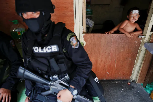 A baby looks at an armed member of a police SWAT team during a drug raid, in Manila, Philippines, October 7, 2016. (Photo by Damir Sagolj/Reuters)