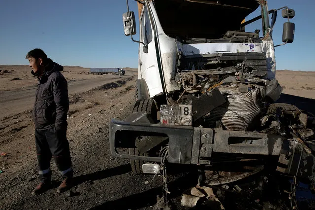 A man stands by a damaged truck after an accident en-route to China in Khanbogd Soum in the Gobi desert, Mongolia, October 29, 2017. Getting to the border can be a harrowing ordeal, as vehicles speed towards China and back down the one-lane road. With no street lamps to guide the way and drink-driving a constant problem, danger levels increase at night, drivers say. (Photo by Bazarsukh Rentsendorj/Reuters)