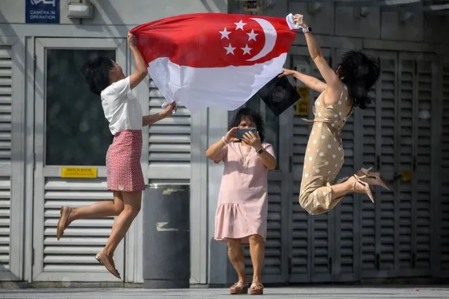 Women holding the Singapore national flag pose for a photograph at the Merlion Park to mark the 55th National Day celebrations in Singapore on August 9, 2020. National Day is celebrated in commemoration of Singapore's independence from Malaysia in 1965. (Photo by Roslan Rahman/AFP Photo)