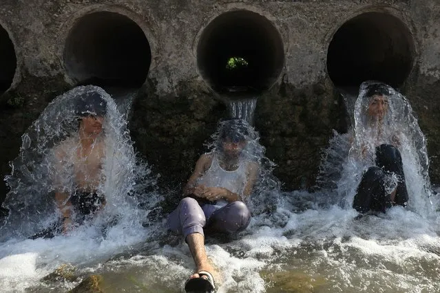People cool off under water pipes from a canal during hot and humid weather, in the outskirts of Peshawar, Pakistan on June 21, 2023. (Photo by Fayaz Aziz/Reuters)
