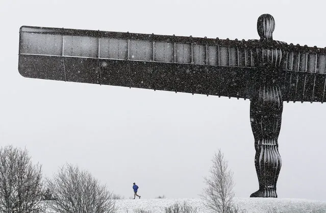 A jogger runs through the snow under the Angel of the North near Gateshead, northeastern England Thursday January 14, 2016, as Britain braced itself for  a new wave of bad weather after forecasters issued warnings of heavy snow in parts of England and Scotland. (Photo by Owen Humphreys/PA Wire via AP Photo)