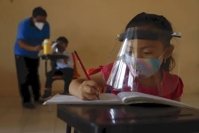 Wearing a mask and a face shield to curb the spread of the new coronavirus, 10-year-old Jade Chan Puc writes in her workbook during the first day of class at the Valentín Gomez Farias Indigenous Primary School in Montebello, Hecelchakan, Campeche state, Monday, April 19, 2021. Campeche is the first state to transition back to the classroom after a year of remote learning due to the pandemic. (Photo by Martin Zetina/AP Photo)