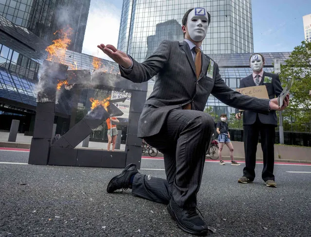 Members of Attac burn down a makeshift Deutsche Bank logo in front of the Deutsche Bank headquarters during the central climate strike of Fridays for Future in Frankfurt, Germany, Friday, August 13, 2021. Several thousand participants attended the protest against the financial sector in the banking city. (Photo by Michael Probst/AP Photo)