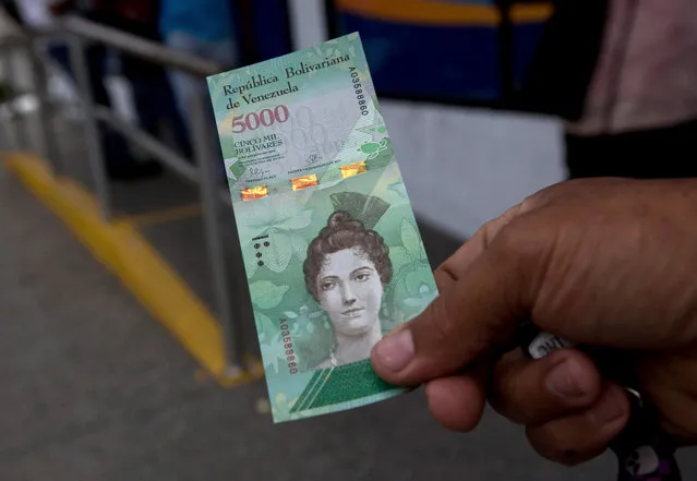 A man shows a new bank note of 5,000 Bolivars outside a bank in Caracas, Venezuela, Monday, January 16, 2017. As the nation experiences triple-digit inflation, the government rolled out larger denomination bank notes on Monday, ranging in value from 500 to 20,000 bolivars. (Photo by Fernando Llano/AP Photo)