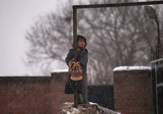 A girl uses a “Kangri”, a traditional fire pot, to warm herself as she holds onto a railing during a snowfall in Srinagar, India January 17, 2017. (Photo by Danish Ismail/Reuters)