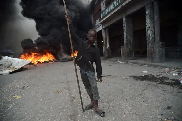 A boy stands before burning tires on the fourth day of protests in Port-au-Prince, on February 10, 2019. Demonstrators are demanding the resignation of Haitian President Jovenel Moise, and protesting the Petrocaribe fund which investigations concluded nearly $2 billion from the program was misused. (Photo by Hector Retamal/AFP Photo)