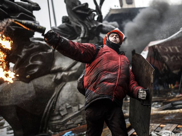 A protester throws a petrol bomb as he stands behind barricades during clashes with police in Kiev, on February 20, 2014. (Photo by Bulent Kilic/AFP Photo)