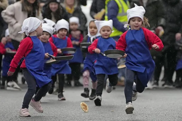 Schoolchildren from local schools take part in the children's races prior to the annual Pancake race in the town of Olney, in Buckinghamshire, England, Tuesday, February 13, 2024. Every year women clad in aprons and head scarves from Olney and the city of Liberal, in Kansas, USA, run their respective legs of the race with pancakes in their pans. According to legend, the Olney race started in 1445 when a harried housewife arrived at church on Shrove Tuesday still clutching her frying pan with a pancake in it. (Photo by Kin Cheung/AP Photo)