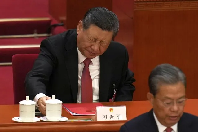 Chinese President Xi Jinping, rear, reacts after drinking from a cup at the closing session of the National People's Congress held at the Great Hall of the People in Beijing, Monday, March 11, 2024. (Photo by Ng Han Guan/AP Photo)