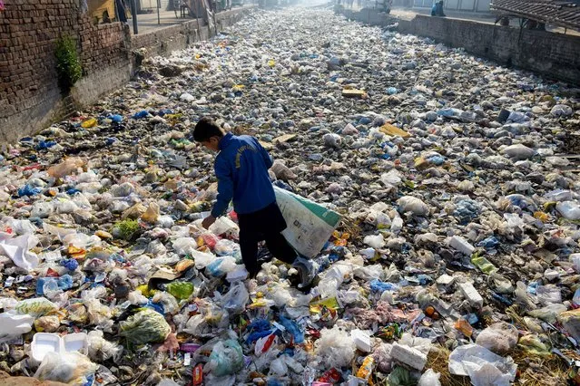 A waste picker scouts for recyclable junk from a sewage drain used as a garbage dump, at a slum area in Lahore on March 4, 2024. (Photo by Syed Murtaza/AFP Photo)