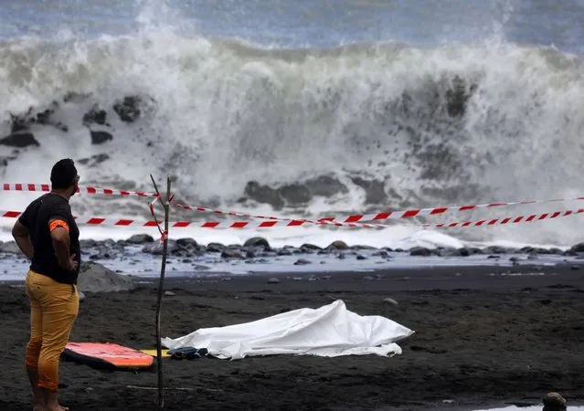 A policeman stands next to the body of a bodyboarder killed by a shark, covered by a white cloth next to his bodyboard on February 21, 2017 on a beach in Saint-Andre, on the French Reunion Island in the Indian Ocean. A 26 year-old bodyboarder was attacked by a shark while bodyboarding in a dangerous water area on February 21, 2017 off Saint-Andre. The man had his femoral artery cut off and bled to death, according to firefighters. (Photo by Richard Bouhet/AFP Photo)