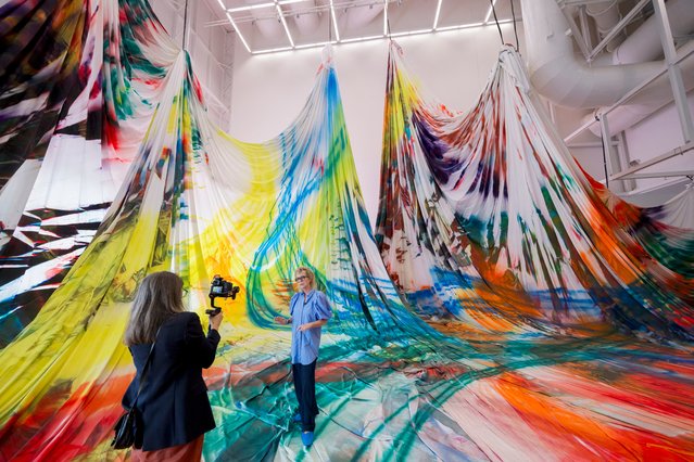 German painter Katharina Grosse (C) is filmed as she stands on her immersive painting “Shifting the stars” during a press preview of “Deplacer les etoiles” (Shifting the stars) exhibition at the Centre Pompidou-Metz in Metz, northeastern France, on May 30, 2024. The exhibition by the German painter, born in 1961 in Freiburg im Breisgau, brings a welcome splash of color to the foot of the Centre Pompidou and its immense, immaculate manta ray-shaped roof until February 24, 2025. (Photo by Jean-Christophe Verhaegen/AFP Photo)