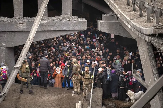 Ukrainians crowd under a destroyed bridge as they try to flee crossing the Irpin river in the outskirts of Kyiv, Ukraine, Saturday, March 5, 2022. (Photo by Emilio Morenatti/AP Photo)