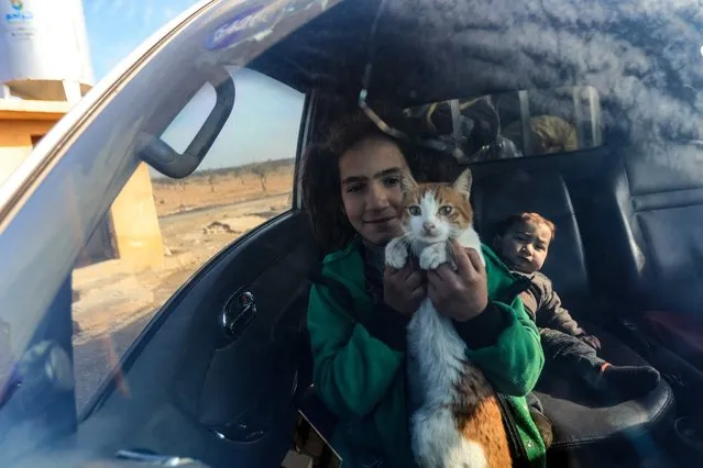 An internally displaced Syrian child holds her cat inside a car at a camp, before being transported to a new housing complex in the opposition-held area of Bizaah, east of the city of al-Bab in the northern Aleppo governorate, built with the support of Turkey's emergencies agency AFAD, on February 9, 2022. A housing complex built for displaced Syrians near the Turkish-held Syrian city of Al-Bab is the latest in a series of residential projects sponsored by Ankara. Turkey's goal is to create a so-called “safe zone” along its border to keep Syrians displaced by war from crossing into its territory, and to allow it to send back some of the millions who already did. (Photo by Bakr Alkasem/AFP Photo)