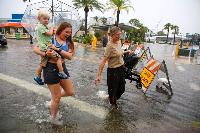 Mabrey Shaffmaster, left, carries her nephew, Arlo Hoggard, as her sister, Morgan Hoggard, carries nine-month-old son Ace Hoggard through a flooded street as Tropical Storm Debby approaches Tarpon Springs, Fla. on August 4, 2024. (Photo by Douglas R. Clifford/Tampa Bay Times/AP Photo)