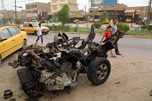 Civilians pass a destroyed car in the a car bomb explosion in southwestern Baghdad, Iraq, Saturday, May 20, 2017. Two car bombs in southwestern Baghdad killed and wounded people and police officers late on Friday night according to Iraqi police and hospital officials. (Photo by Karim Kadim/AP Photo)