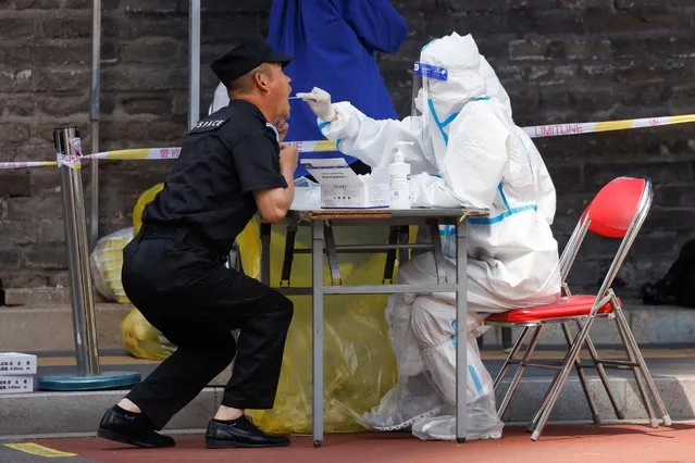 A medical worker in a protective suit collects a swab sample from a man at a makeshift nucleic acid testing site amid the coronavirus disease (COVID-19) outbreak in Beijing, China on May 11, 2022. (Photo by Carlos Garcia Rawlins/Reuters)