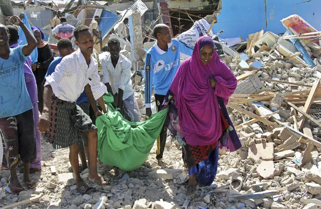 Somalis carry away the body of a civilian who was killed in a car bomb attack in Mogadishu, Somalia Tuesday, June 20, 2017. A number of people are dead after a suicide car bomber in a vehicle posing as a milk delivery van detonated at a district headquarters in Somalia's capital, police said Tuesday. (Photo by Farah Abdi Warsameh/AP Photo)