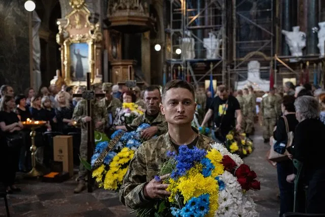 A Ukrainian soldier carries flowers in the national colors, of blue and yellow, as the Ukrainian Army buries with military honors three of its soldiers, each of whom died fighting invading Russian forces at frontlines across the country, in the Saints Peter and Paul Garrison Church in Lviv, Ukraine, on June 18, 2022. The three soldiers - Oleksii Tarasiev, Rostyslav Tymkiv, and Ihor Skakun - are among the 100 to 200 Ukrainian servicemen that Ukrainian officials say are dying each day on frontlines, mostly in the eastern Donbas region, which Russia has been bombarding for months with artillery and rocket attacks in a bid to seize control of eastern Ukraine. (Photo by Scott Peterson/Getty Images)