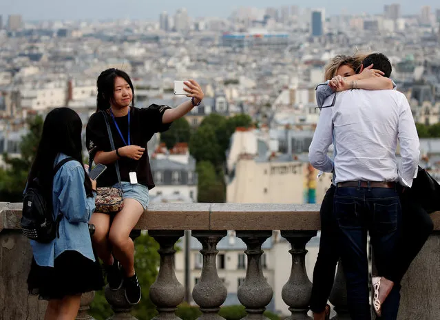 A couple embraces while tourists take selfies on a sightseeing point overlooking Paris, next to the Sacre Coeur (Sacred Heart) basilica, France, July 31, 2017. (Photo by Christian Hartmann/Reuters)