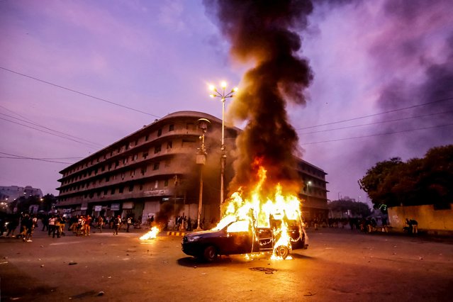 Smoke plumes from a police vehicle set on fire by members and supporters of the Tehreek-e-Labbaik Pakistan (TLP) party during a protest in Karachi on October 13, 2024. Eleven Pakistan police officers have been suspended for the “mistreatment” of protesters, officials said on October 14, after videos showed women being roughly handled including one dragged away by her hands and feet. Competing protests over the incendiary charge of blasphemy were held in the mega city of Karachi on October 13, despite not having permission from authorities, when clashes broke out. (Photo by Qaisar Khan/AFP Photo)