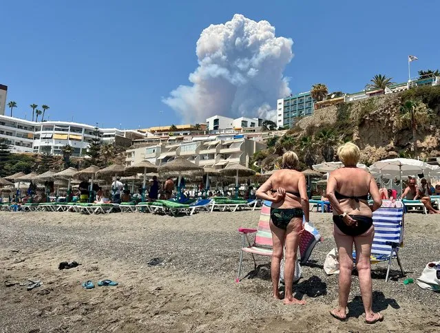 People look at plumes of smoke caused by a wildfire in Malaga, seen from Playa del Bajondillo beach in Torremolinos, Spain, July 15, 2022. (Photo by Hannah McKay/Reuters)