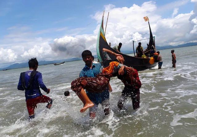 Smoke is seen on Myanmar's side of border as an exhausted Rohingya refugee woman is carried to the shore after crossing the Bangladesh-Myanmar border by boat through the Bay of Bengal, in Shah Porir Dwip, Bangladesh September 11, 2017. (Photo by Danish Siddiqui/Reuters)