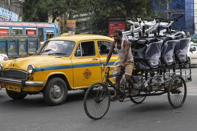 A delivery man pedals his transport rickshaw loaded with office chairs past an Ambassador taxi in Kolkata, India, Tuesday, August 23, 2022. (Photo by Bikas Das/AP Photo)