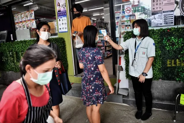 A 7-11 convenience store employee takes the temperature of a customer, in an effort to contain the spread of the COVID-19 coronavirus, in Bangkok on April 10, 2020. (Photo by Lillian Suwanrumpha/AFP Photo)