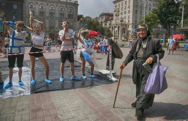 Young people perform a routine to attract public attention to the problem of human trafficking, as an elderly woman passes by, during a protest in central Kiev, Ukraine, Friday, July 29, 2016. The United Nations General Assembly has declared July 30 as World Day against Trafficking in Persons. (Photo by Efrem Lukatsky/AP Photo)