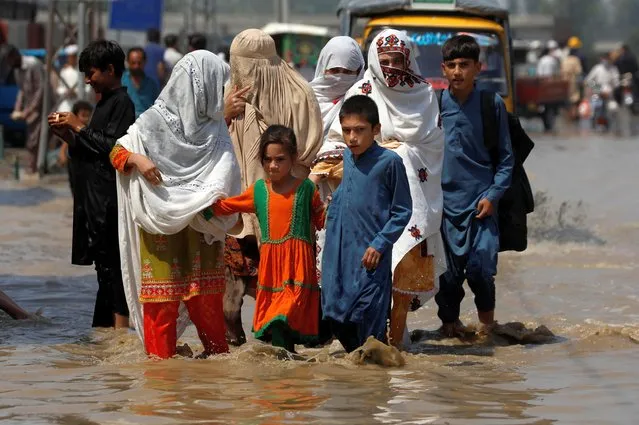 A family walk along a flooded street, following rains and floods during the monsoon season in Nowshera, Pakistan on August 30, 2022. (Photo by Fayaz Aziz/Reuters)