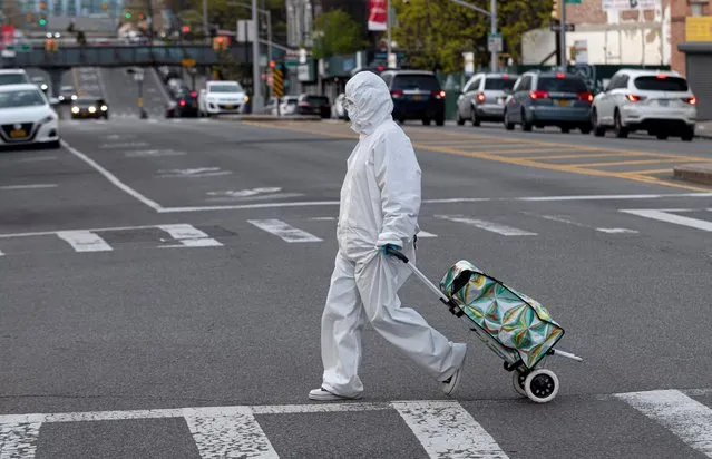 A woman wearing a hazmat suit and googles pulls her grocery cart in the streets in Queens, a borough of New York City amid the coronavirus pandemic on April 20, 2020 in New York City. (Photo by Johannes Eisele/AFP Photo)