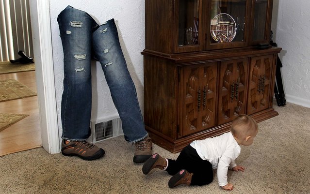 Chloe Mills, 1-year-old daughter of Army Staff Sgt. Travis Mills and his wife Kelsey, crawls past her father's walking legs in his boyhood home in Vassar, Michigan, on October 4, 2012. Mills is visiting his hometown for the first time since losing all four limbs while fighting in Afghanistan.(Photo by Carlos Osorio/Associated Press)