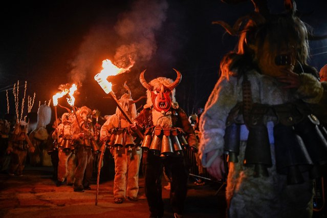Bulgarian dancers wearing costumes perform a ritual dance with flaming torches during the Kukeri Carnival in the village of Batanovtsi, western Bulgaria, on January 13, 2024. The Kukeri Carnival is a festival of brightly colored masks and costumes which marks the beginning of Spring. Every participant makes his own multi-colored personal mask, covered with beads, ribbons and woolen tassels. The heavy swaying of the main mummer is meant to represent wheat heavy with grain, and the bells tied around the waist are intended to drive away the evil spirits and the sickness. (Photo by Nikolay Doychinov/AFP Photo)