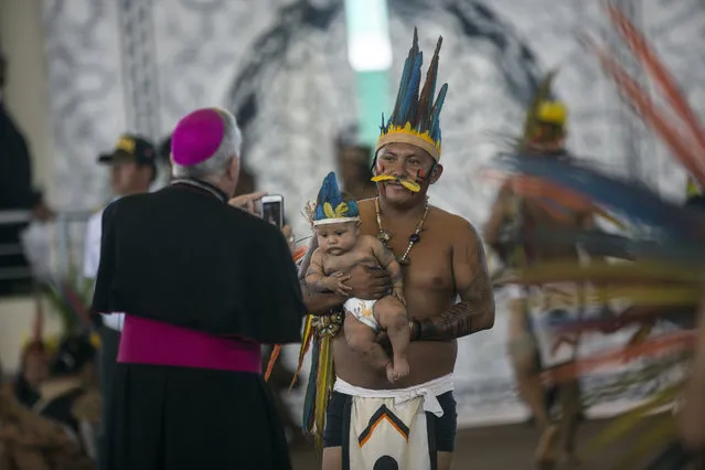 A bishop takes a photo of an indigenous man and baby as they wait for the arrival of Pope Francis in Puerto Maldonado, Madre de Dios province, Peru, Friday, January 19, 2018. After lengthy treks through the muddy Amazon, indigenous men, women and children will greet Francis Friday in a visit to the world's largest rainforest that native leaders hope will mark a turning point for the increasingly threatened ecosystem. (Photo by Rodrigo Abd/AP Photo)