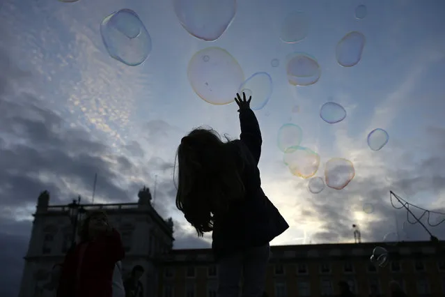A little girl tries to reach soap bubbles made by a street artist at the Comercio square, in Lisbon, Portugal, Saturday, November 15,2014. (Photo by Francisco Seco/AP Photo)