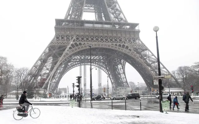 A man rides bicycle as he makes his way along a snow-covered sidewalk near the Eiffel Tower in Paris March 12, 2013 as winter weather with snow and freezing temperatures returns to northern France. (Photo by John Schults/Reuters)