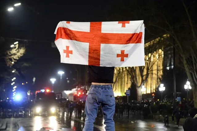 A protester holds a Georgian national flag standing in front of a police line outside the Georgian parliament building in Tbilisi, Georgia, Thursday, March 9, 2023. (Phoot by AP Photo/Stringer)