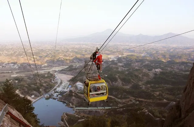 An employee of Shiniuzhai Scenic Resort dressed as Santa Claus hangs beside a cable car as he presents gifts to visitors, in Pingjiang, Hunan province, December 20, 2014. (Photo by Reuters/Stringer)