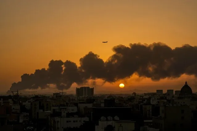 A passenger airplane flies over a smoldering fire at a Saudi Aramco oil depot after a Yemen Houthi rebel attack, ahead of a Formula One race as the sun rises in Jiddah, Saudi Arabia, Saturday, March 26, 2022. (Photo by Hassan Ammar/AP Photo)