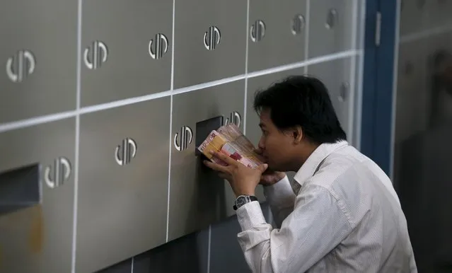 An employee of a money changer passes a stack of Indonesia rupiah notes through small window to his  colleague in Jakarta, in this October 8, 2015 file photo. Indonesia's foreign currency reserves have doubled in size in the eight years since the global financial crisis roiled its markets but an examination by Reuters of its reserve assets shows a thinner buffer than officially reported data on gross reserves suggests. (Photo by Reuters/Beawiharta)